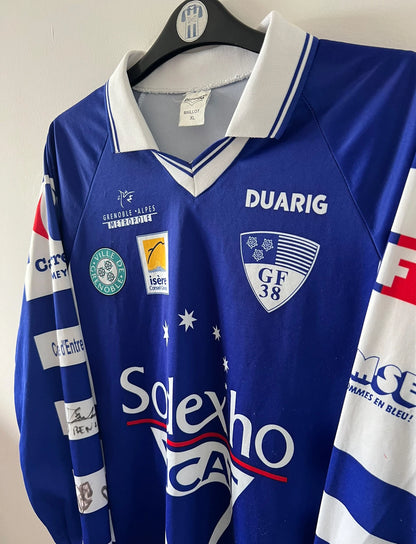 Maillot de foot vintage domicile bleu et blanc de Grenoble de la saison 1999/2000. On peut retrouver l'équipementier Duarig et l'équipementier Sodexho. Il s'agit d'un maillot authentique d'époque.