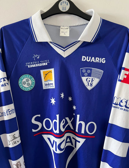 Maillot de foot vintage domicile bleu et blanc de Grenoble de la saison 1999/2000. On peut retrouver l'équipementier Duarig et l'équipementier Sodexho. Il s'agit d'un maillot authentique d'époque.