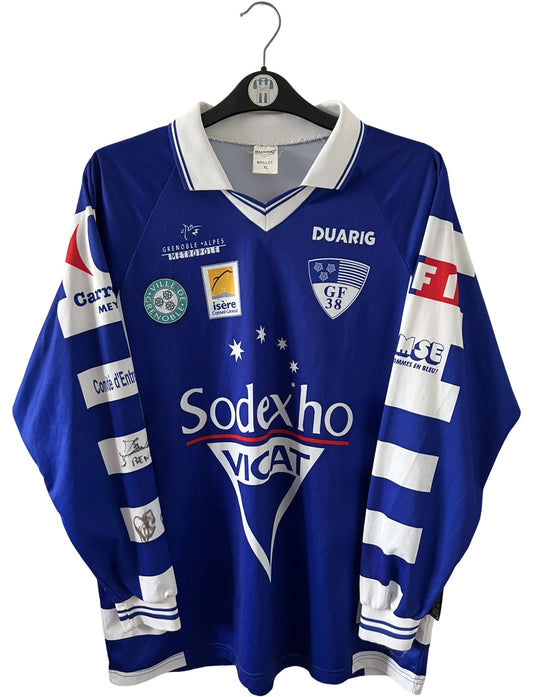 Maillot de foot vintage domicile bleu et blanc de Grenoble de la saison 1999/2000. On peut retrouver l'équipementier Duarig et l'équipementier Sodexho. Il s'agit d'un maillot authentique d'époque.