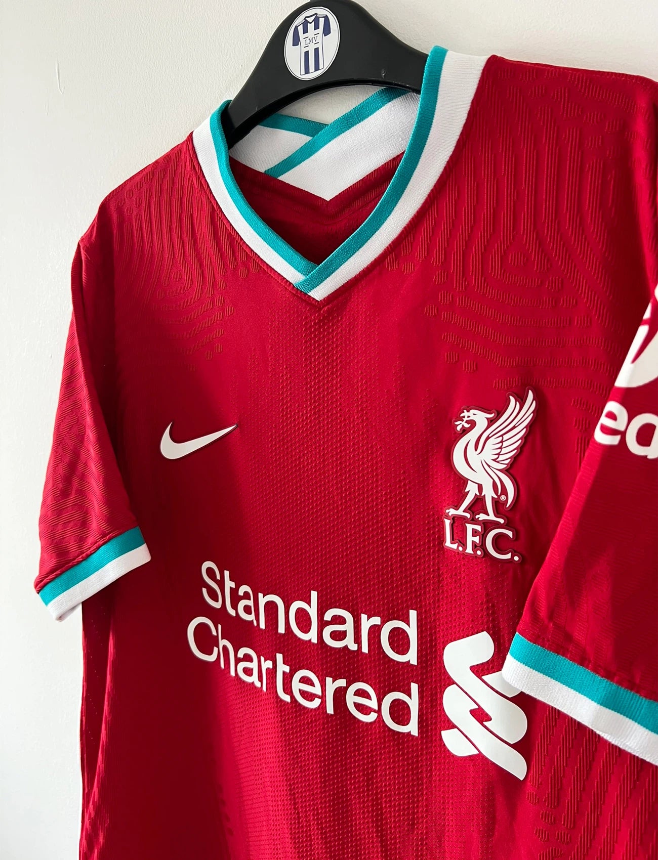 Maillot de foot vintage domicile rouge de Liverpool 2020/2021 en version vapor. On peut retrouver l'équipementier Nike et le sponsor Standard Chartered. Il s'agit d'un maillot authentique d'époque.