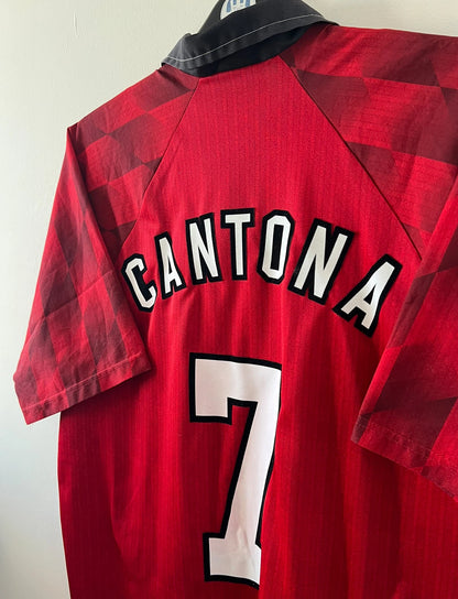 Maillot de foot vintage domicile rouge de Manchester United 1996/1998. On peut retrouver l'équipementier Umbro et le sponsor Sharp. Le maillot est floqué du numéro 7 Eric Cantona. Il s'agit d'un maillot authentique d'époque.