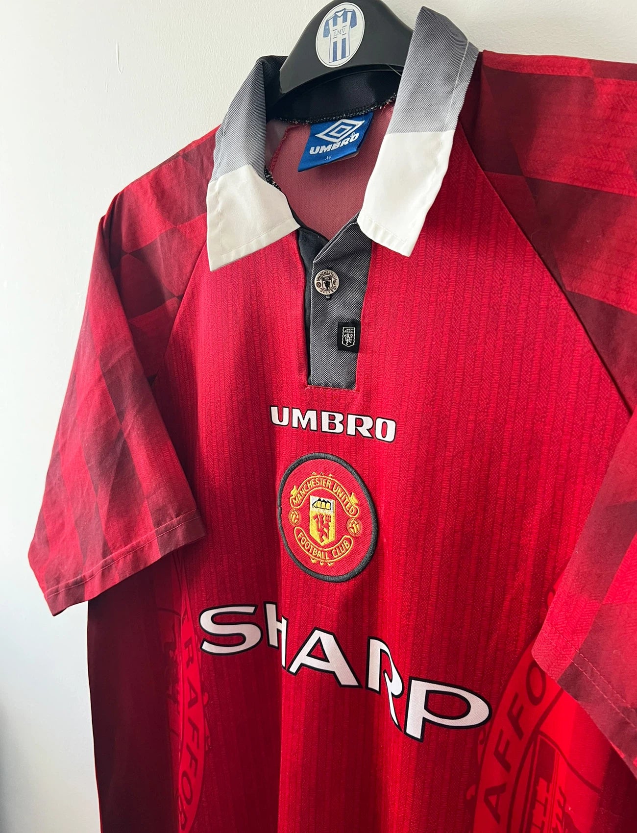 Maillot de foot vintage domicile rouge de Manchester United 1996/1998. On peut retrouver l'équipementier Umbro et le sponsor Sharp. Le maillot est floqué du numéro 7 Eric Cantona. Il s'agit d'un maillot authentique d'époque.