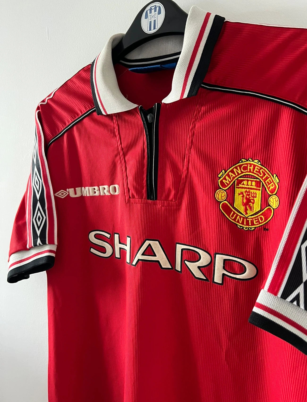 Maillot de foot vintage domicile rouge de Manchester United saison 1998/2000. On peut retrouver l'équipementier Umbro et le sponsor Sharp. Il s'agit d'un maillot authentique d'époque.