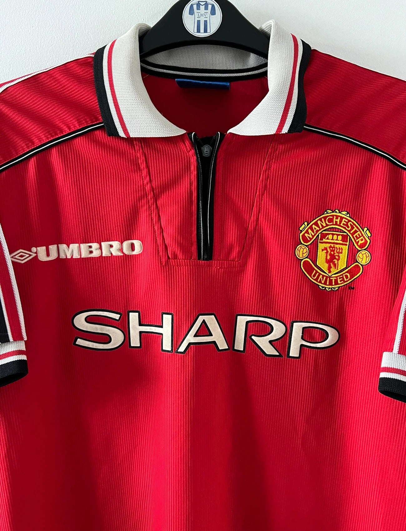 Maillot de foot vintage domicile rouge de Manchester United saison 1998/2000. On peut retrouver l'équipementier Umbro et le sponsor Sharp. Il s'agit d'un maillot authentique d'époque.