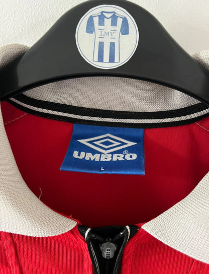 Maillot de foot vintage domicile rouge de Manchester United saison 1998/2000. On peut retrouver l'équipementier Umbro et le sponsor Sharp. Il s'agit d'un maillot authentique d'époque.