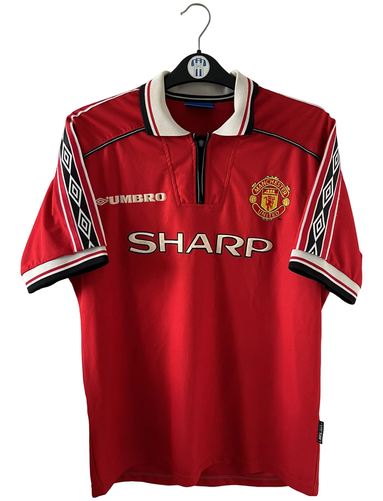 Maillot de foot vintage domicile rouge de Manchester United saison 1998/2000. On peut retrouver l'équipementier Umbro et le sponsor Sharp. Il s'agit d'un maillot authentique d'époque.