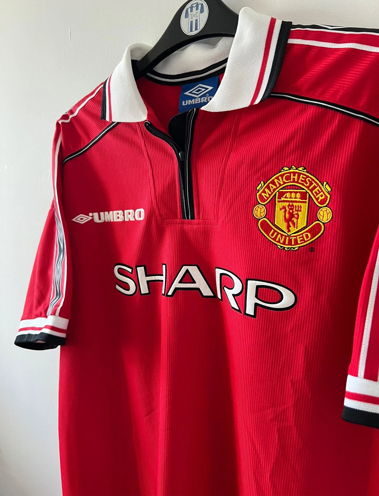 Maillot de foot vintage domicile rouge de Manchester United saison 1998/2000. On peut retrouver l'équipementier Umbro et le sponsor Sharp. Il s'agit d'un maillot authentique d'époque.
