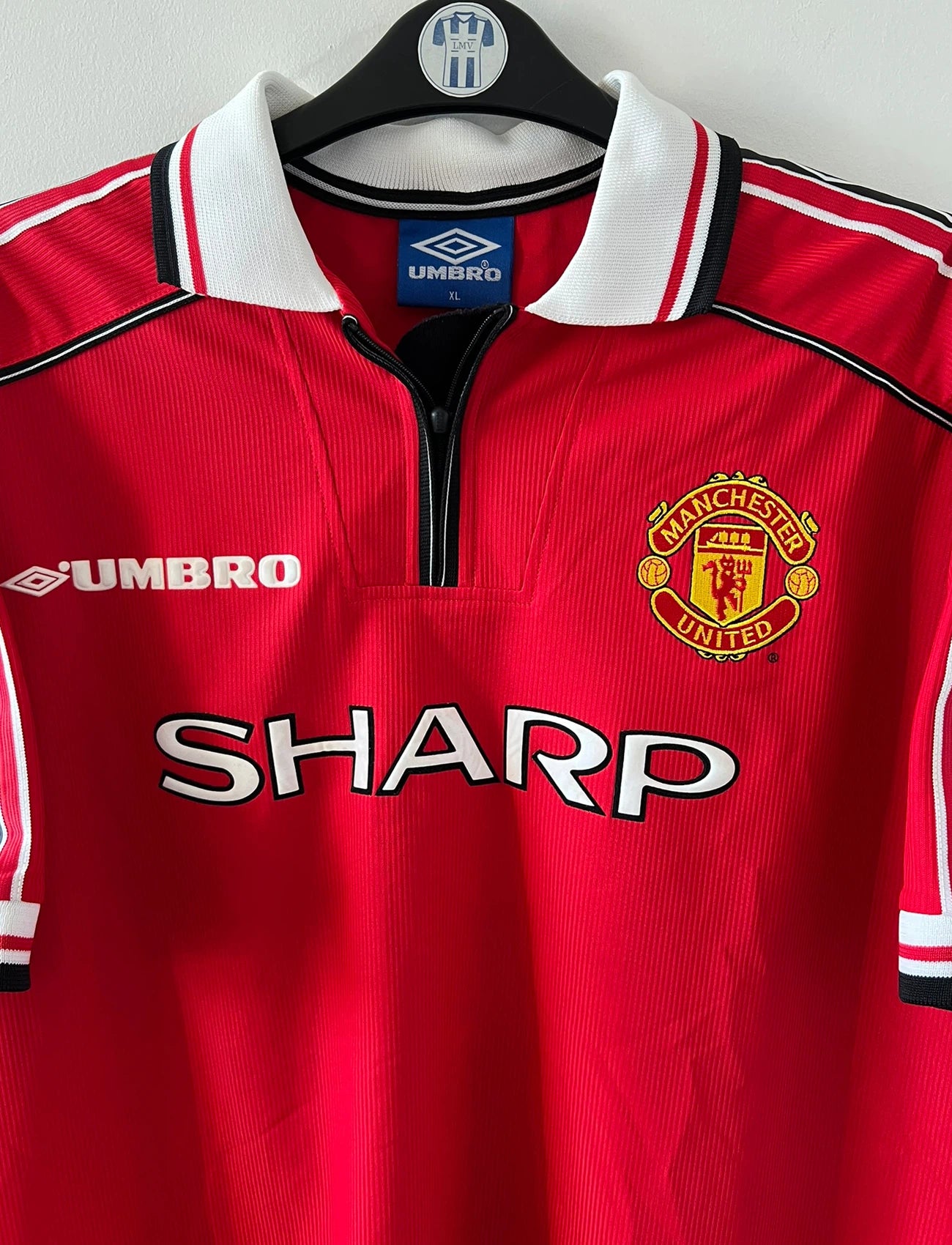 Maillot de foot vintage domicile rouge de Manchester United saison 1998/2000. On peut retrouver l'équipementier Umbro et le sponsor Sharp. Il s'agit d'un maillot authentique d'époque.