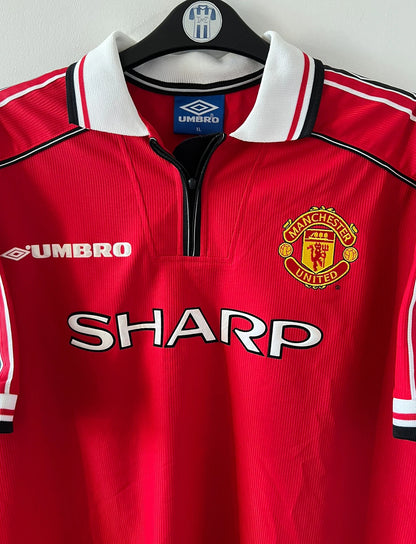 Maillot de foot vintage domicile rouge de Manchester United saison 1998/2000. On peut retrouver l'équipementier Umbro et le sponsor Sharp. Il s'agit d'un maillot authentique d'époque.