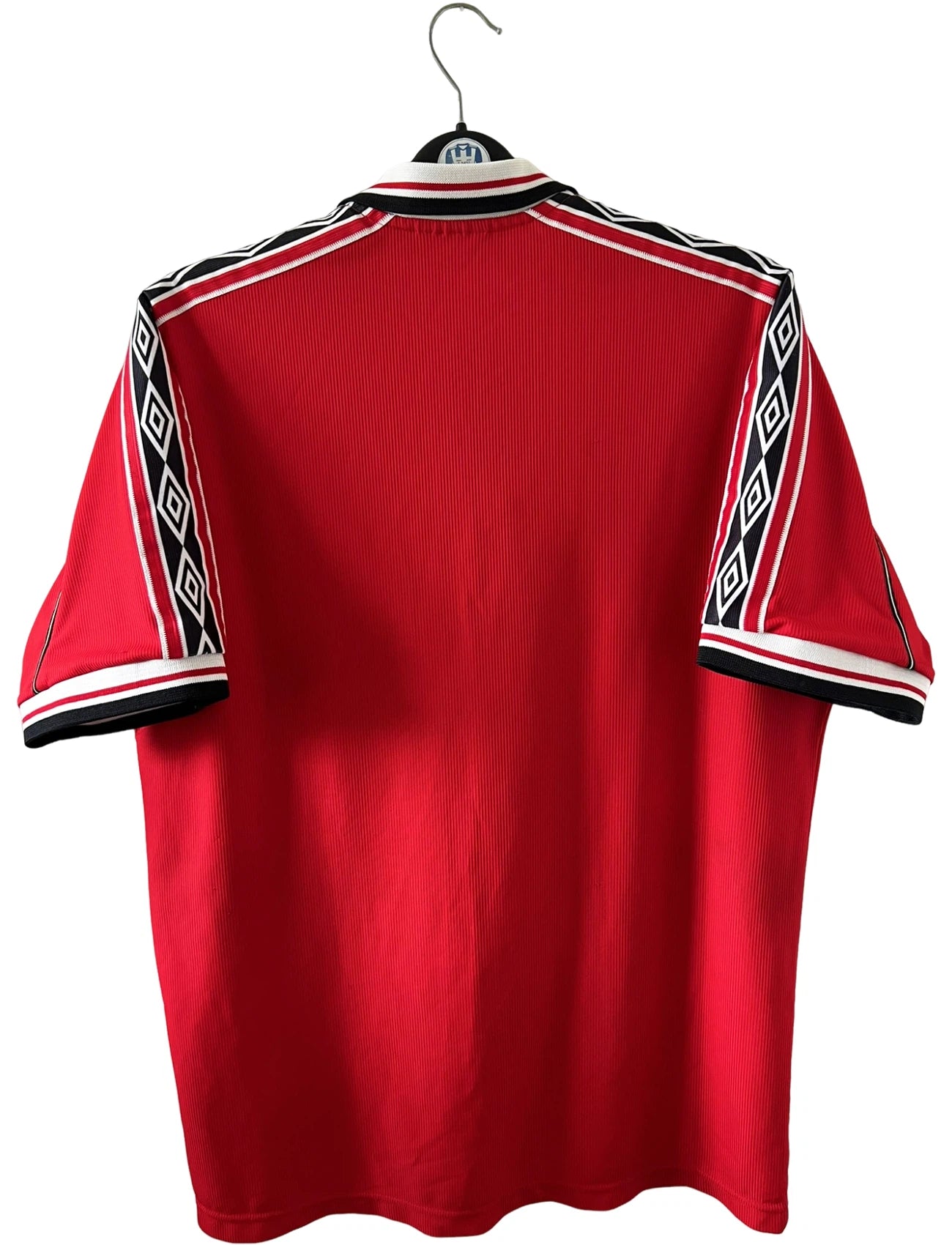 Maillot foot vintage domicile rouge de Manchester United 1998. On peut retrouver l'équipementier Umbro et le sponsor Sharp. Il s'agit d'un maillot authentique d'époque.