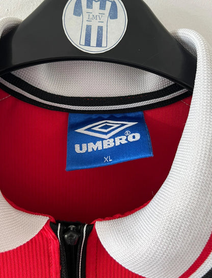 Maillot foot vintage domicile rouge de Manchester United 1998. On peut retrouver l'équipementier Umbro et le sponsor Sharp. Il s'agit d'un maillot authentique d'époque.