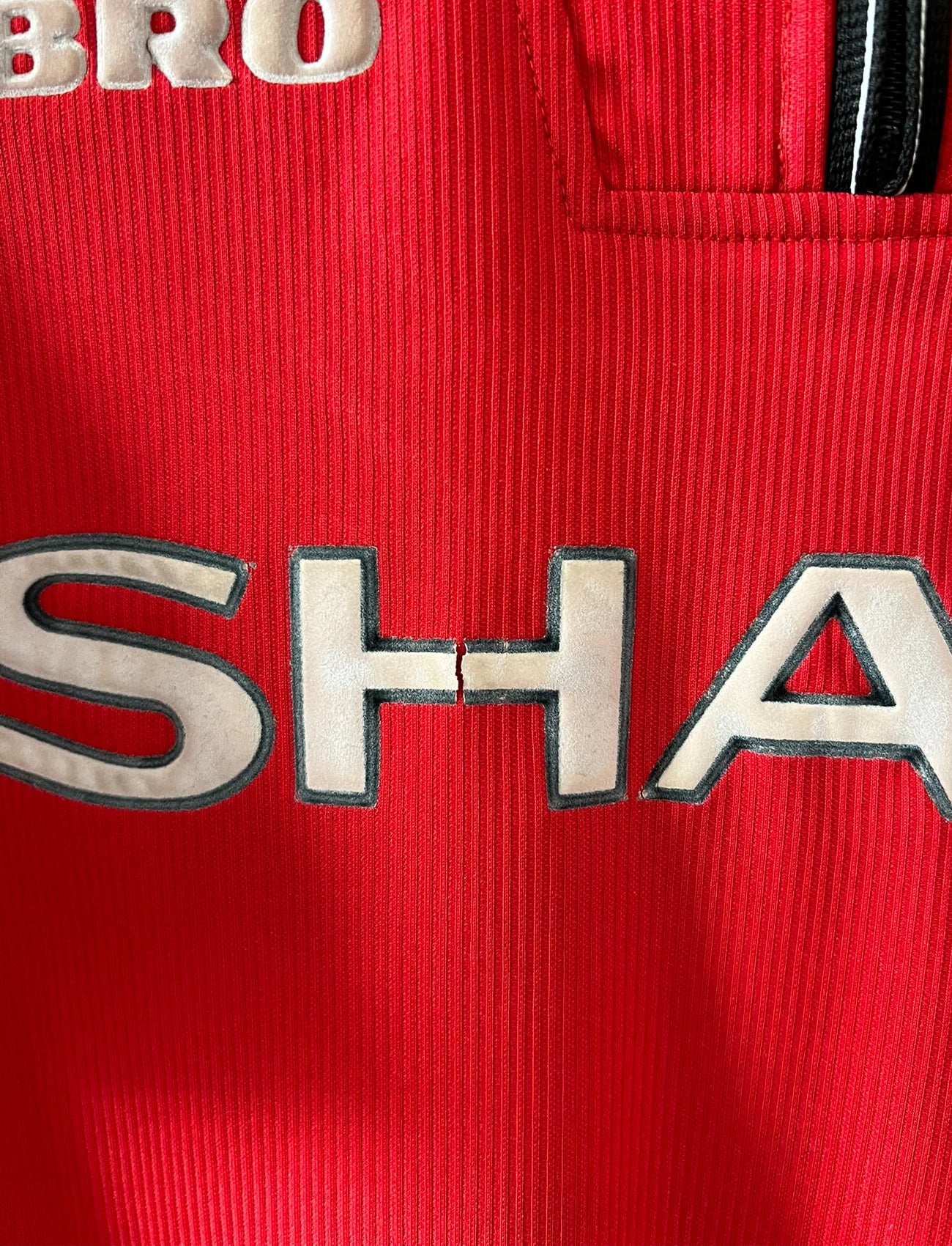 Maillot foot vintage domicile rouge de Manchester United 1998. On peut retrouver l'équipementier Umbro et le sponsor Sharp. Il s'agit d'un maillot authentique d'époque.