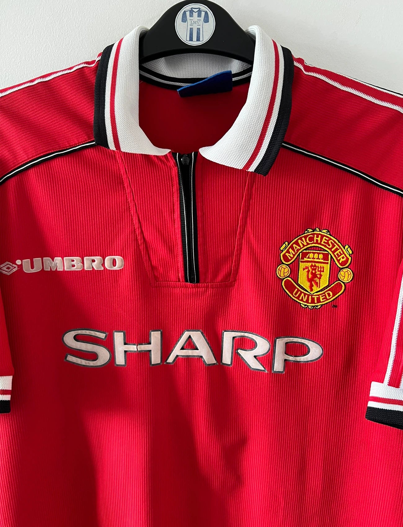 Maillot foot vintage domicile rouge de Manchester United 1998. On peut retrouver l'équipementier Umbro et le sponsor Sharp. Il s'agit d'un maillot authentique d'époque.