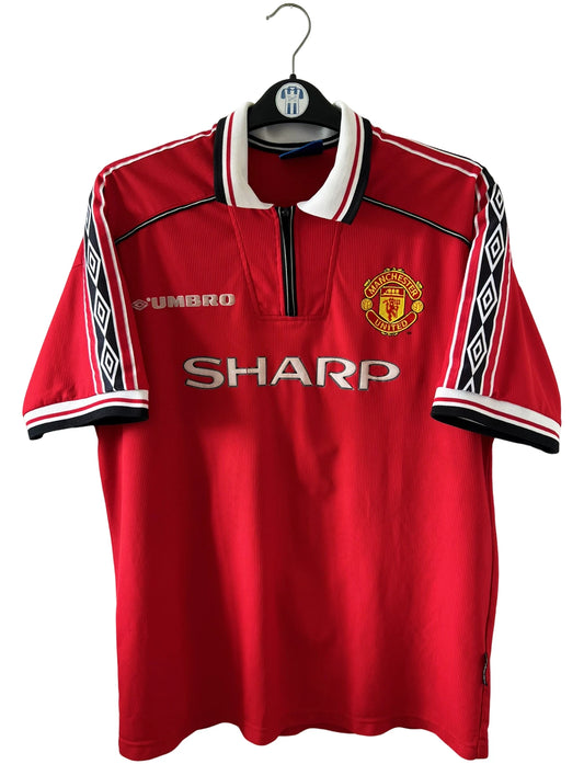 Maillot foot vintage domicile rouge de Manchester United 1998. On peut retrouver l'équipementier Umbro et le sponsor Sharp. Il s'agit d'un maillot authentique d'époque.