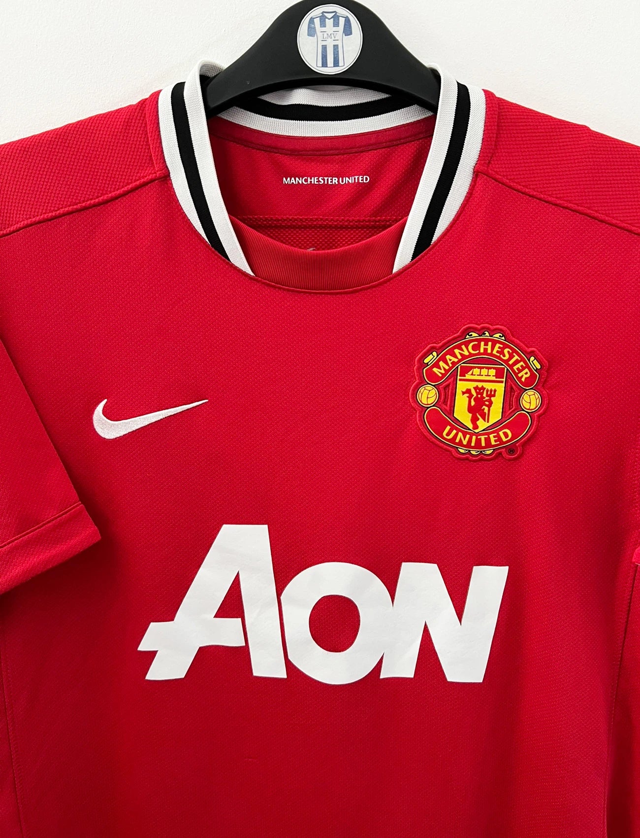 Maillot de foot vintage domicile rouge de Manchester United 2011/2012. On peut retrouver l'équipementier Nike et le sponsor Aon. Il s'agit d'un maillot authentique d'époque.
