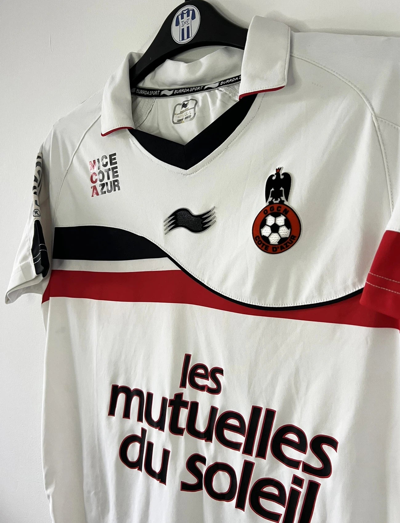 Maillot de foot vintage extérieur blanc de l'OGC Nice porté par Fabian Monzon lors de la saison 2011/2012. On peut retrouver l'équipementier Burrda Sport et le sponsor Mutuelle du Soleil. Le maillot est floqué du numéro 18 Fabian Monzon. Il s'agit d'un maillot authentique d'époque.