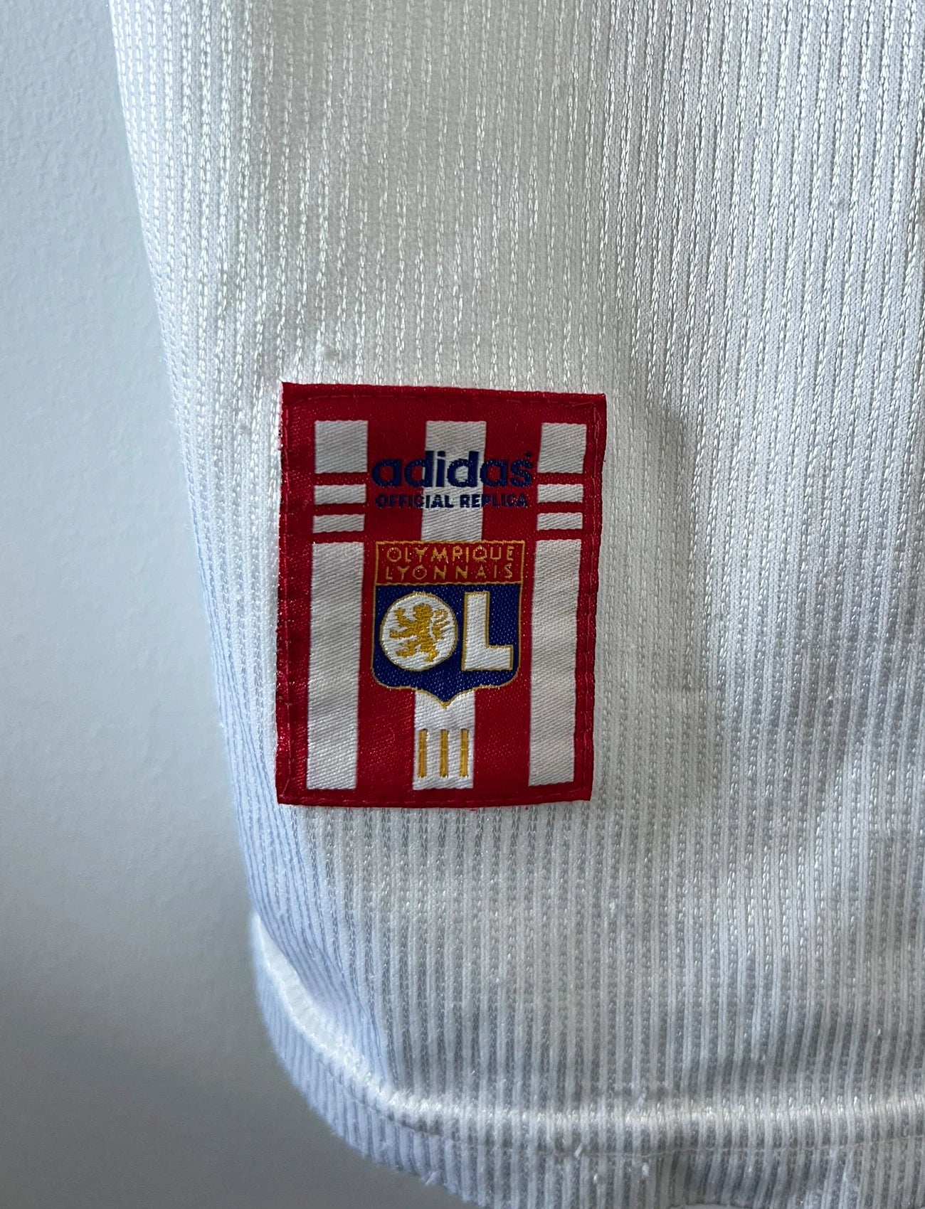 Maillot de foot vintage domicile blanc de l'OL 1999/2000. On peut retrouver l'équipementier Adidas et le sponsor Pathé. Le maillot est floqué du numéro 9 Sonny Anderson. Il s'agit d'un maillot authentique d'époque