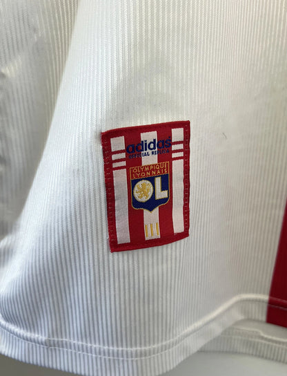 Maillot de foot vintage domicile blanc, bleu et rouge de l'Olympique Lyonnais de la saison 1998/2000. On peut retrouver l'équipementier Adidas et le sponsor Infogrames. Il s'agit d'un maillot authentique d'époque.
