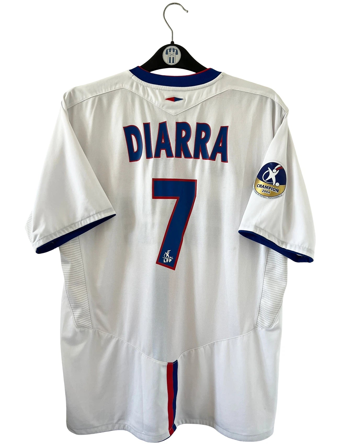 Maillot de foot vintage domicile blanc de l'OL de la saison 2004/2005. On peut retrouver l'équipementier Umbo et le sponsor Renault Trucks. Le maillot est floqué du numéro 7 Mahamadou Diarra. Il s'agit d'un maillot authentique d'époque.
