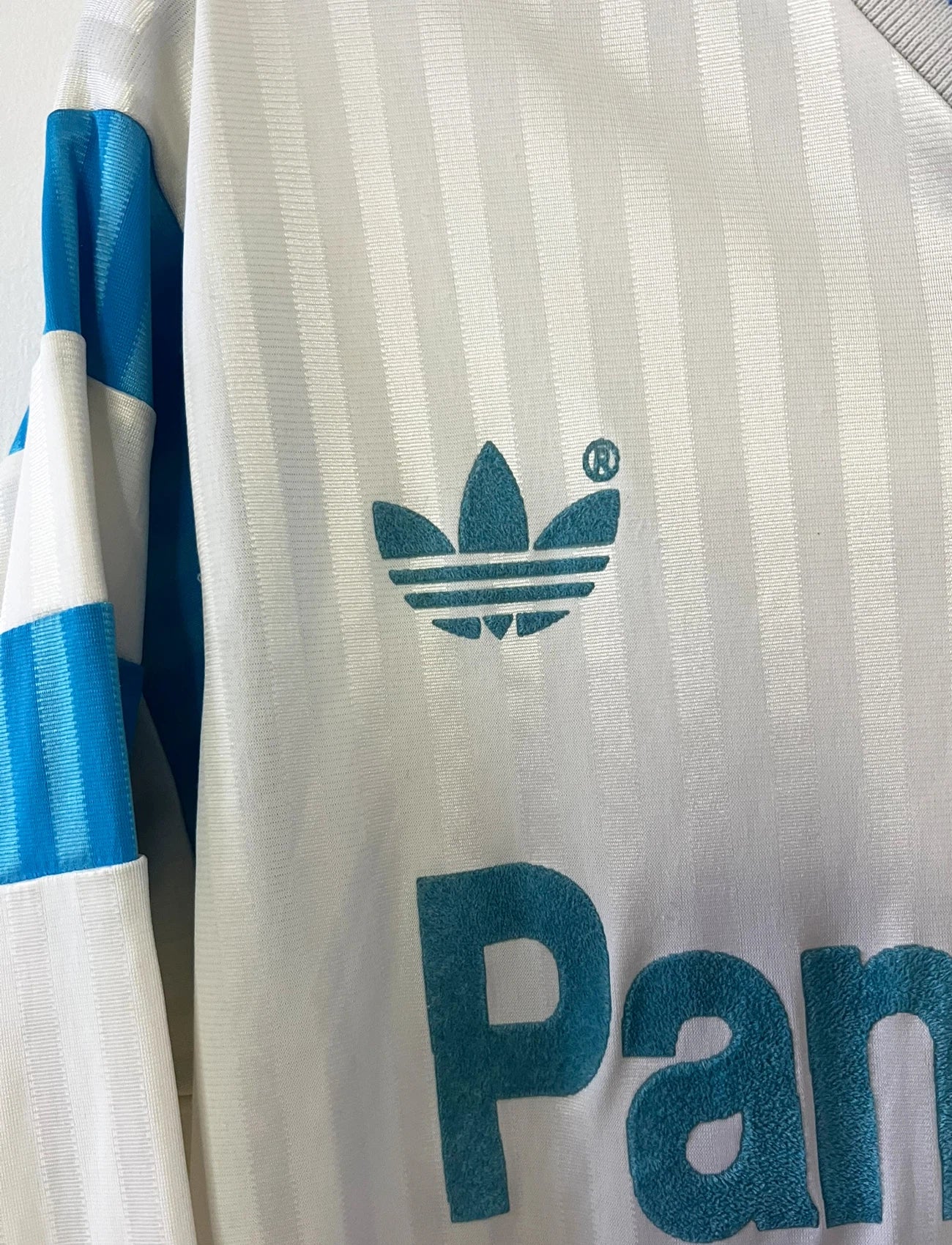 Maillot de foot vintage domicile blanc de l'OM 1989/1991. On peut retrouver l'équipementier Adidas et le sponsor Panasonic. Il s'agit d'un maillot authentique d'époque.