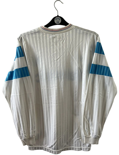 Maillot de foot vintage domicile blanc et bleu de l'om 1989/1991. On peut retrouver l'équipementier Adidas et le sponsor Panasonic. Il s'agit d'un maillot authentique d'époque.