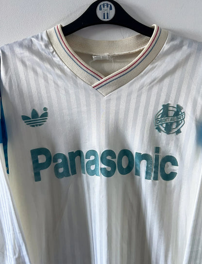 Maillot foot vintage domicile blanc de l'OM 1989/1991. On peut retrouver l'équipementier Adidas et le sponsor Panasonic. Il s'agit d'un maillot authentique d'époque.
