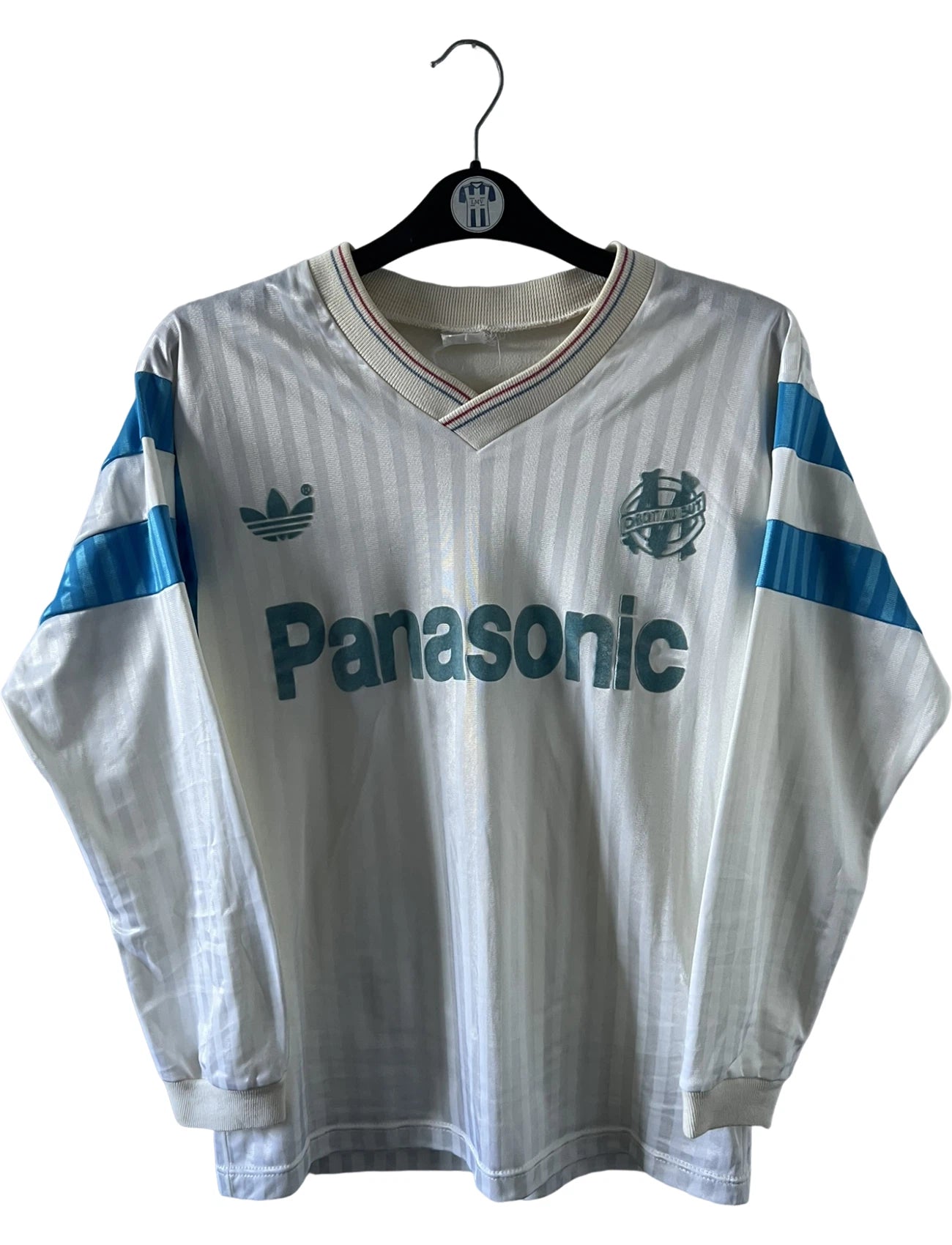 Maillot foot vintage domicile blanc de l'OM 1989/1991. On peut retrouver l'équipementier Adidas et le sponsor Panasonic. Il s'agit d'un maillot authentique d'époque.