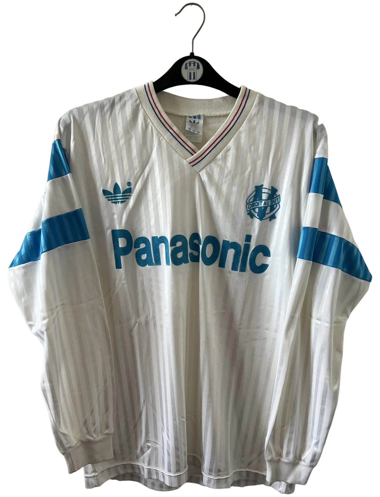 Maillot de foot vintage domicile blanc et bleu de l'om 1989/1991. On peut retrouver l'équipementier Adidas et le sponsor Panasonic. Il s'agit d'un maillot authentique d'époque.