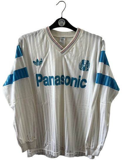 Maillot de foot vintage domicile blanc et bleu de l'om 1989/1991. On peut retrouver l'équipementier Adidas et le sponsor Panasonic. Il s'agit d'un maillot authentique d'époque.