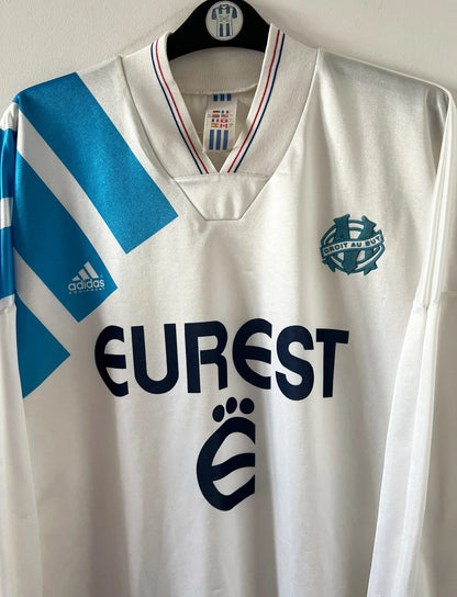 Maillot de foot vintage domicile blanc et bleu de l'OM 1992/1993. On peut retrouver l'équipementier Adidas et le sponsor Eurest. Il s'agit d'un maillot authentique d'époque.