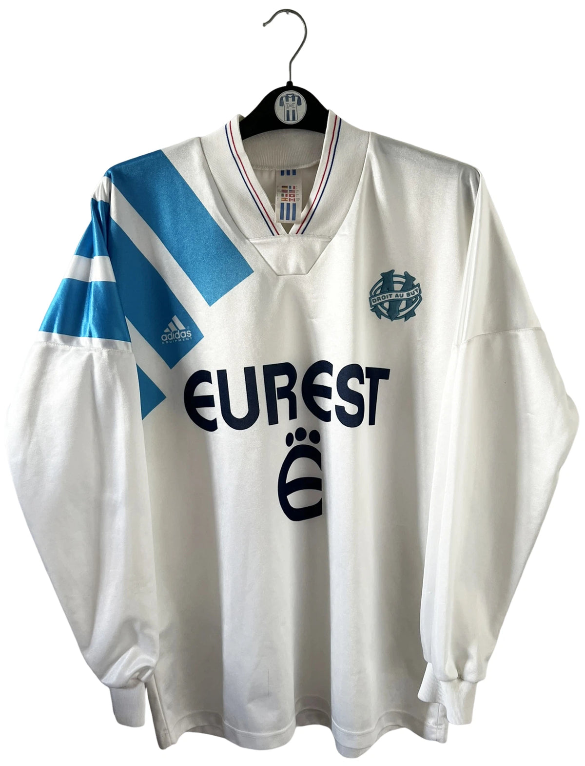 Maillot de foot vintage domicile blanc et bleu de l'OM 1992/1993. On peut retrouver l'équipementier Adidas et le sponsor Eurest. Il s'agit d'un maillot authentique d'époque.