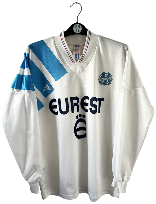 Maillot de foot vintage domicile blanc et bleu de l'OM 1992/1993. On peut retrouver l'équipementier Adidas et le sponsor Eurest. Il s'agit d'un maillot authentique d'époque.