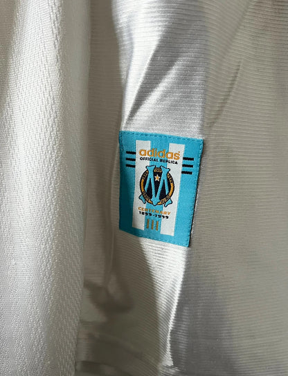Maillot de foot vintage domicile blanc de l'OM 1998/1999. On peut retrouver l'équipementier Adidas et le sponsor Ericsson. Il s'agit d'un maillot authentique d'époque.
