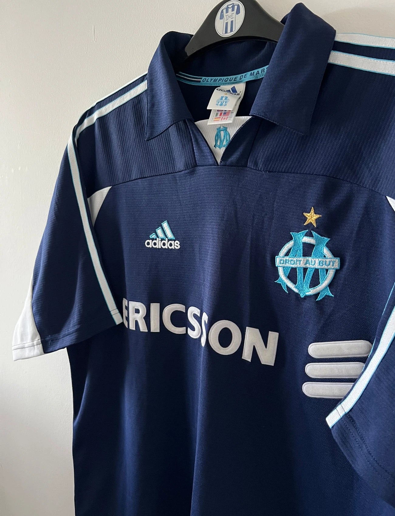 Maillot de foot vintage OM 1999/2000 extérieur bleu. On peut retrouver l'équipementier Adidas et le sponsor Ericsson. Il s'agit d'un maillot authentique d'époque.