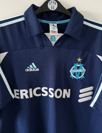 Maillot de foot vintage OM 1999/2000 extérieur bleu. On peut retrouver l'équipementier Adidas et le sponsor Ericsson. Il s'agit d'un maillot authentique d'époque.