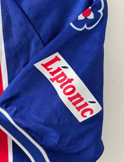 Maillot de foot vintage domicile bleu et rouge du PSG 1994/1995. On peut retrouver l'équipementier Nike et les sponsor SEAT, Tourtel et Liptonic. Il s'agit d'un maillot authentique d'époque.