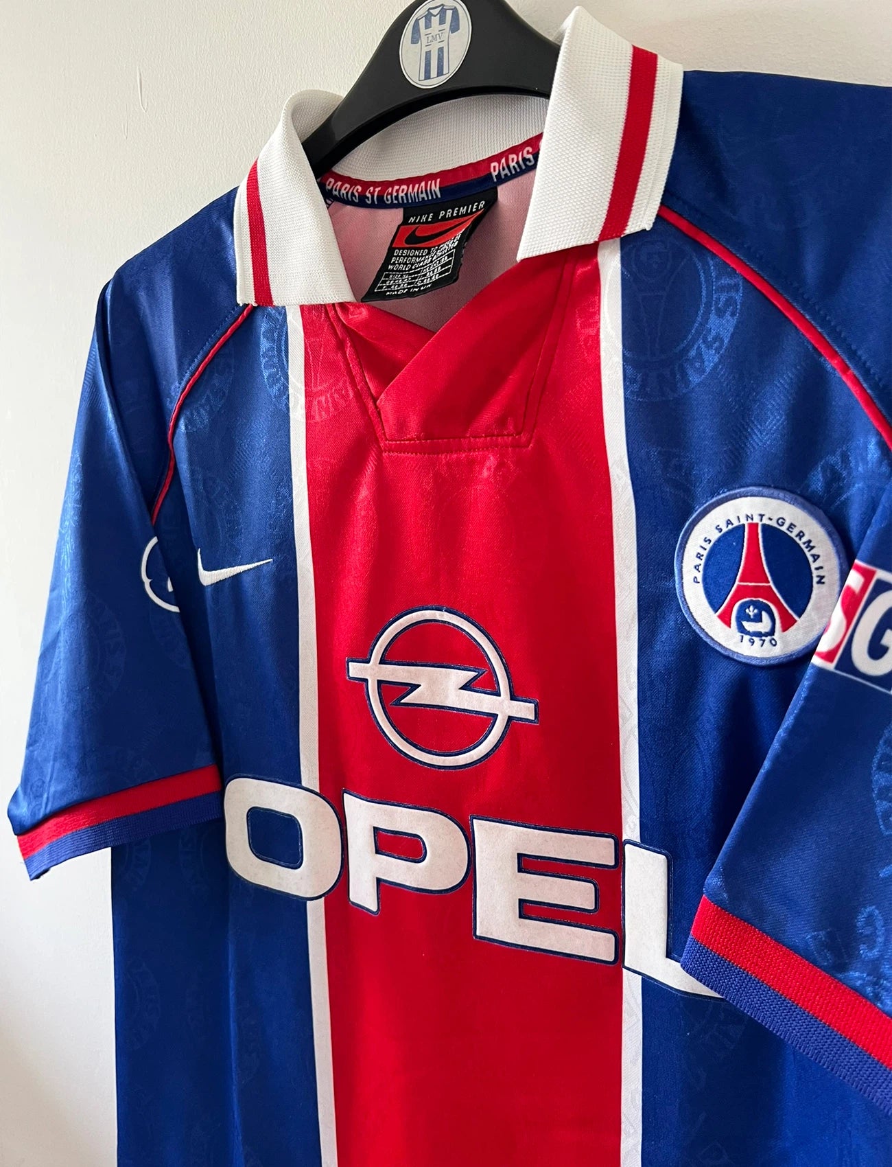 Maillot de foot vintage domicile rouge et bleu du PSG de la saison 1996/1997. On peut retrouver la fameuse bande hechter avec l'équipementier Nike et le sponsor Opel. Il s'agit d'un maillot authentique d'époque.