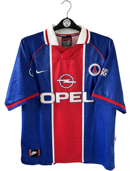 Maillot de foot vintage domicile rouge et bleu du PSG de la saison 1996/1997. On peut retrouver la fameuse bande hechter avec l'équipementier Nike et le sponsor Opel. Il s'agit d'un maillot authentique d'époque.