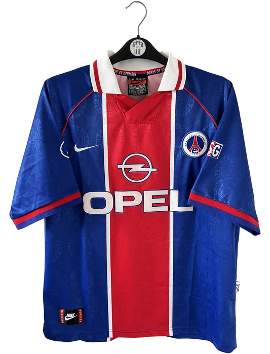 Maillot de foot vintage domicile rouge et bleu du PSG de la saison 1996/1997. On peut retrouver la fameuse bande hechter avec l'équipementier Nike et le sponsor Opel. Il s'agit d'un maillot authentique d'époque.