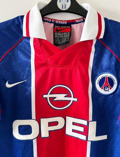 Maillot de foot vintage domicile bleu et rouge du PSG 1996/1997. On peut retrouver l'équipementier Nike et le sponsor OPEL. Il s'agit d'un maillot authentique d'époque.