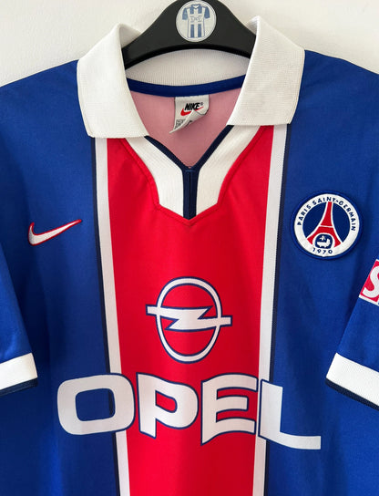 Maillot de foot vintage domicile bleu et rouge du PSG de la saison 1997/1998. On peut retrouver l'équipementier Nike et le sponsor Opel. Il s'agit d'un maillot authentique d'époque.
