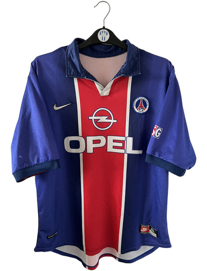 Maillot de foot vintage domicile bleu et rouge du PSG 1998/1999. On peut retrouver l'équipementier Nike et le sponsor Opel. Il s'agit d'un maillot authentique d'époque.