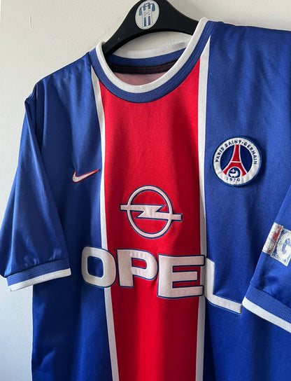 Maillot de foot vintage domicile rouge et bleu du PSG 1999/2000. On peut retrouver l'équipementier Nike et le sponsor OPEL. Il s'agit d'un maillot authentique d'époque.