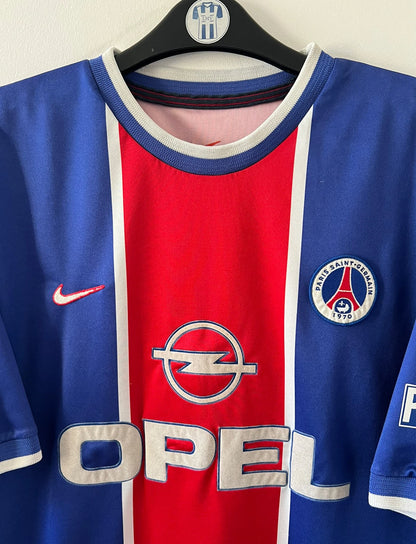 Maillot de foot vintage domicile bleu et rouge du PSG 1999/2000. On peut retrouver l'équipementier Nike et le sponsor Opel. Il s'agit d'un maillot authentique d'époque.