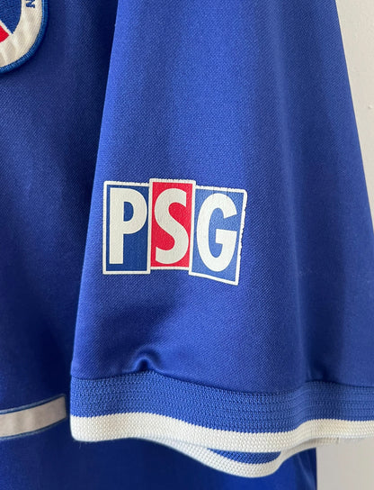Maillot de foot vintage domicile bleu et rouge du PSG 1999/2000. On peut retrouver l'équipementier Nike et le sponsor Opel. Il s'agit d'un maillot authentique d'époque.