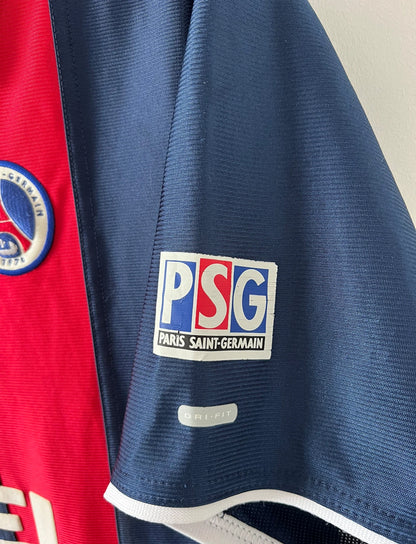 Maillot de foot vintage domicile bleu et rouge du PSG 2001/2002. On peut retrouver l'équipementier Nike et le sponsor Opel. Il s'agit d'un maillot authentique d'époque.