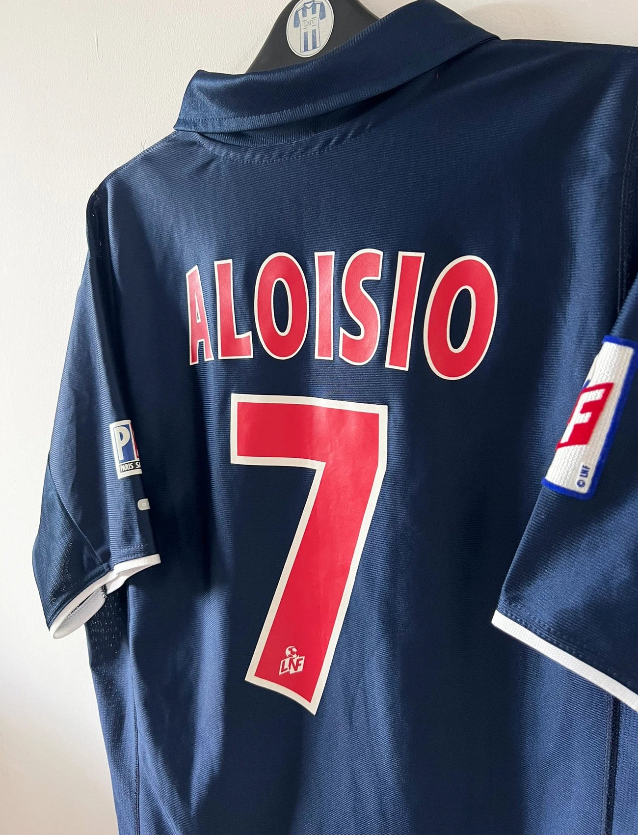 Maillot de foot vintage domicile bleu du PSG 2001/2002. On peut retrouver l'équipementier Nike et le sponsor Opel. Le maillot est floqué du numéro 7 Aloisio. Il s'agit d'un maillot authentique d'époque.