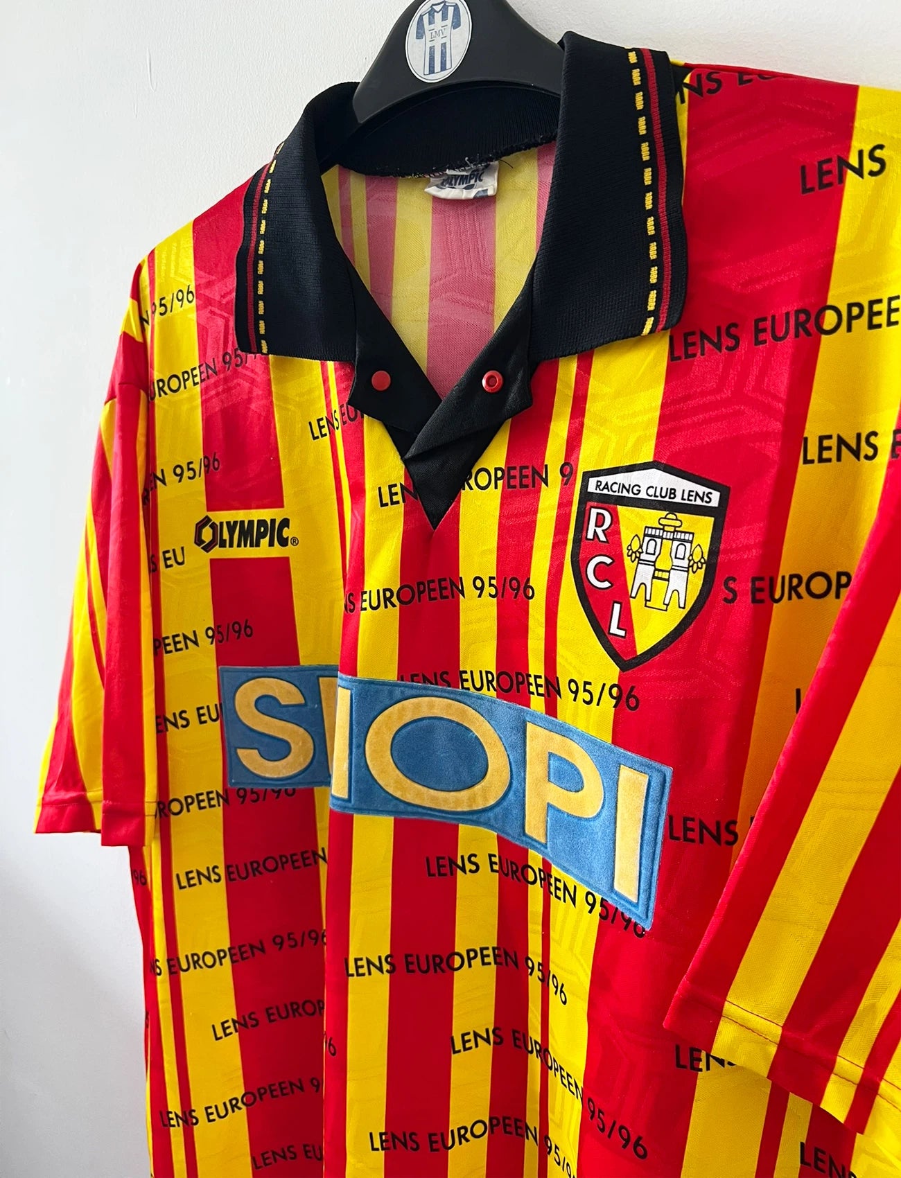 Maillot de foot vintage domicile jaune et rouge du RC Lens 1995/1996. Il s'agit d'une version Lens Européen 95/96. On peut retrouver l'équipementier Olympic et le sponsor Shopi. Il s'agit d'un maillot authentique d'époque.