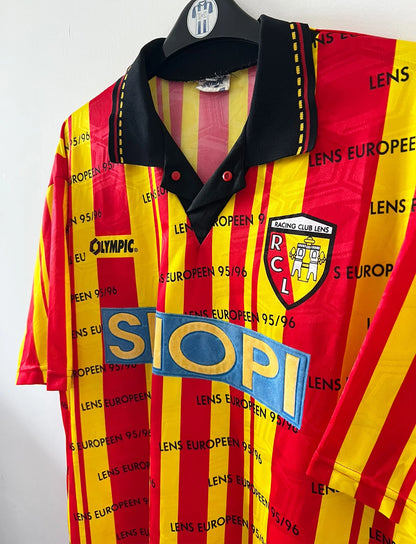 Maillot de foot vintage domicile jaune et rouge du RC Lens 1995/1996. Il s'agit d'une version Lens Européen 95/96. On peut retrouver l'équipementier Olympic et le sponsor Shopi. Il s'agit d'un maillot authentique d'époque.