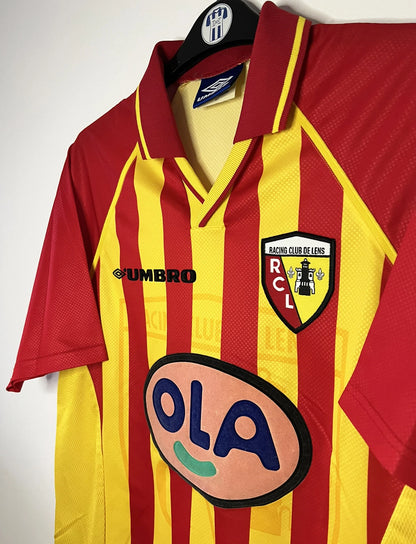 Maillot de foot vintage domicile jaune et rouge du RC Lens de la saison 1998/1999. On peut retrouver l'équipementier Umbro et le sponsor OLA. Il s'agit d'un maillot authentique d'époque.